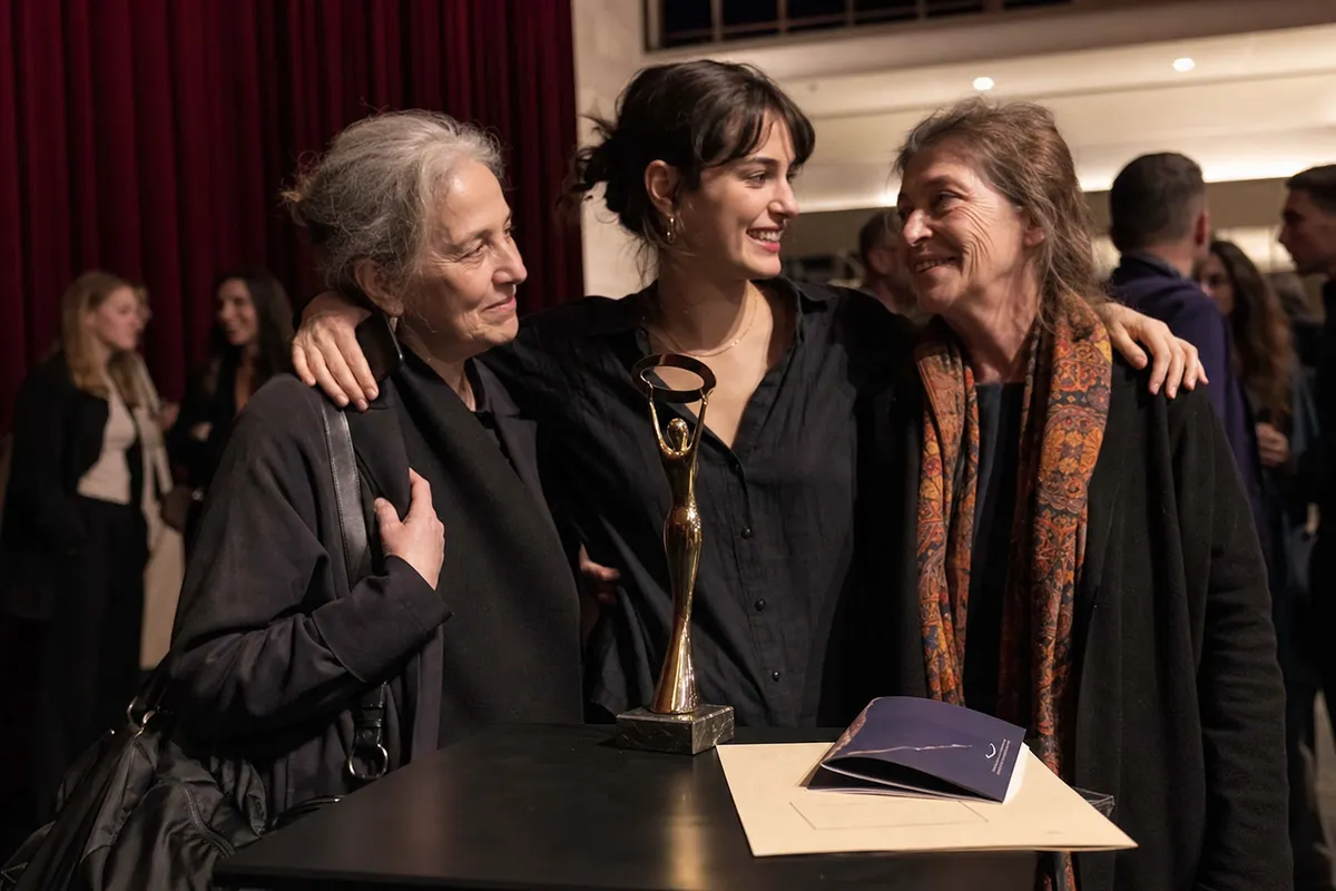 Tre donne si abbracciano accanto a un trofeo su un tavolo dopo una cerimonia in un festival cinematografico