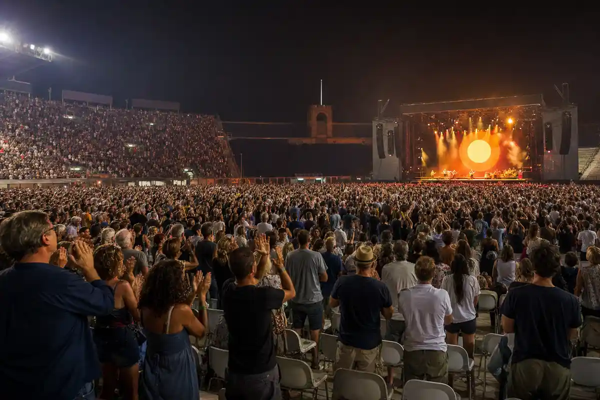 Folla in uno stadio di notte durante un concerto, con palco illuminato e grande cerchio luminoso sullo sfondo